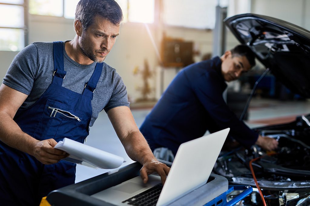 Two auto repairmen working on a car with diagnostic computer Technicians working on client car